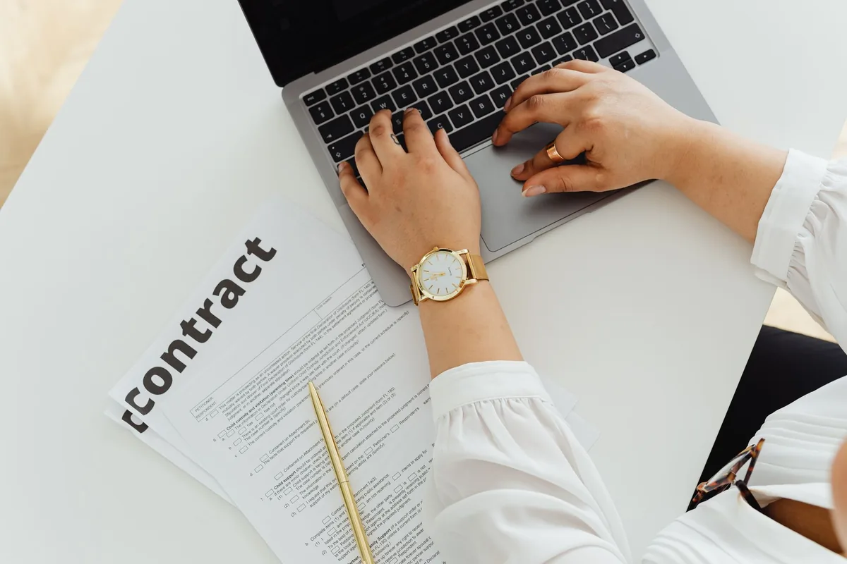 Freelance signant un contrat de prestation de service sur son bureau avec un ordinateur portable